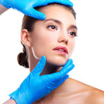 Studio shot of a beautiful young woman getting her face analyzed by gloved hands against a beige background