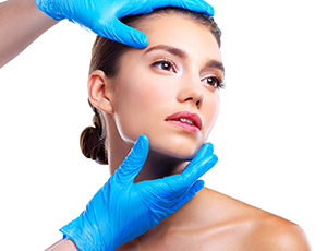 Studio shot of a beautiful young woman getting her face analyzed by gloved hands against a beige background